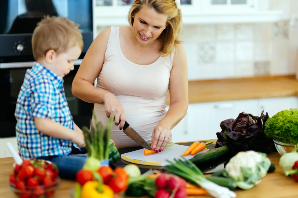 pregnant mother with son cutting vegetables
