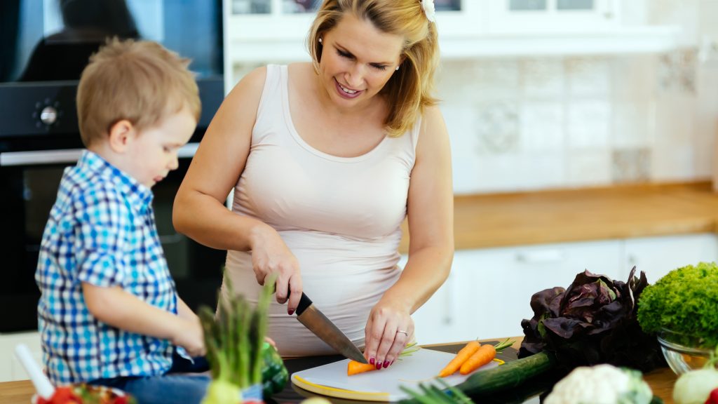 Pregnant mother with son cutting vegetables