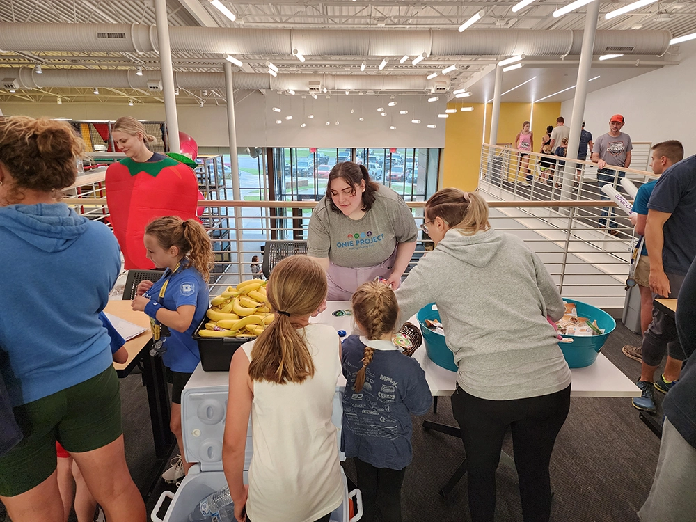 A group of WOW participants crowds in front of the ONIE-sponsored snacks table featuring fresh fruits.