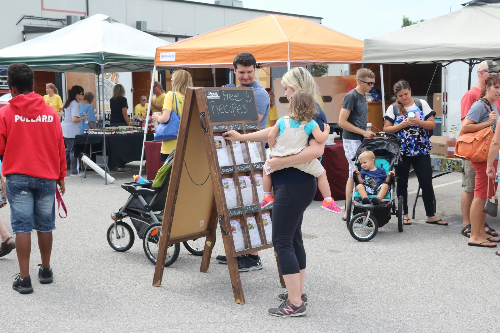 A family examines the free recipes handout station at a local farmers market.