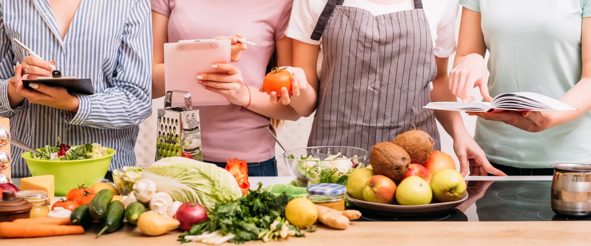 A table of produce is shown with a few people who are taking notes and inspecting the table.