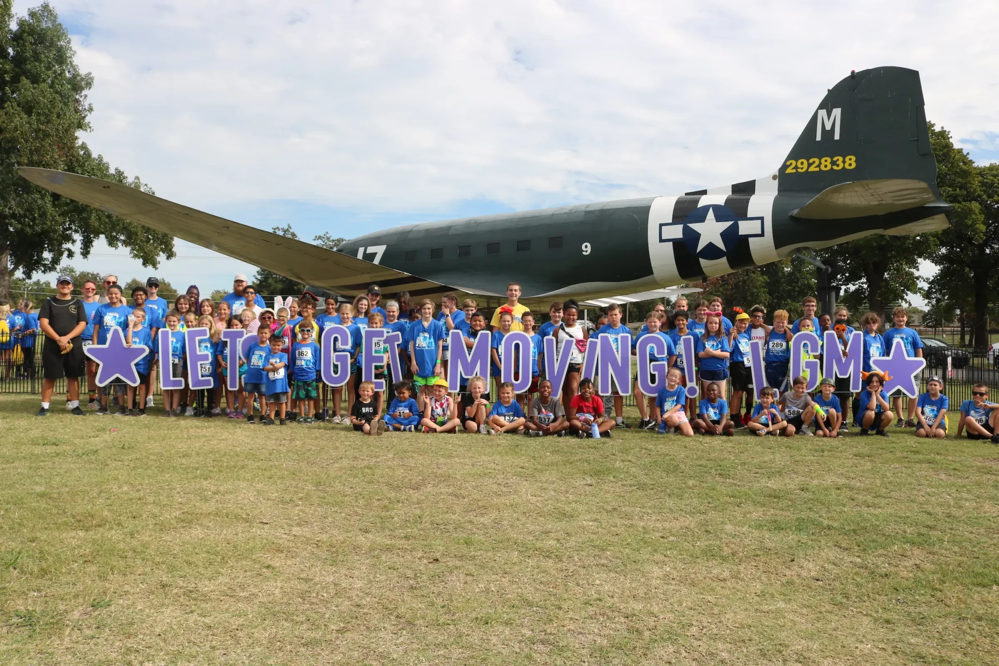 A large group of Let's Get Midwest City Movers standing in front of a plane at the 2023 LGM event.