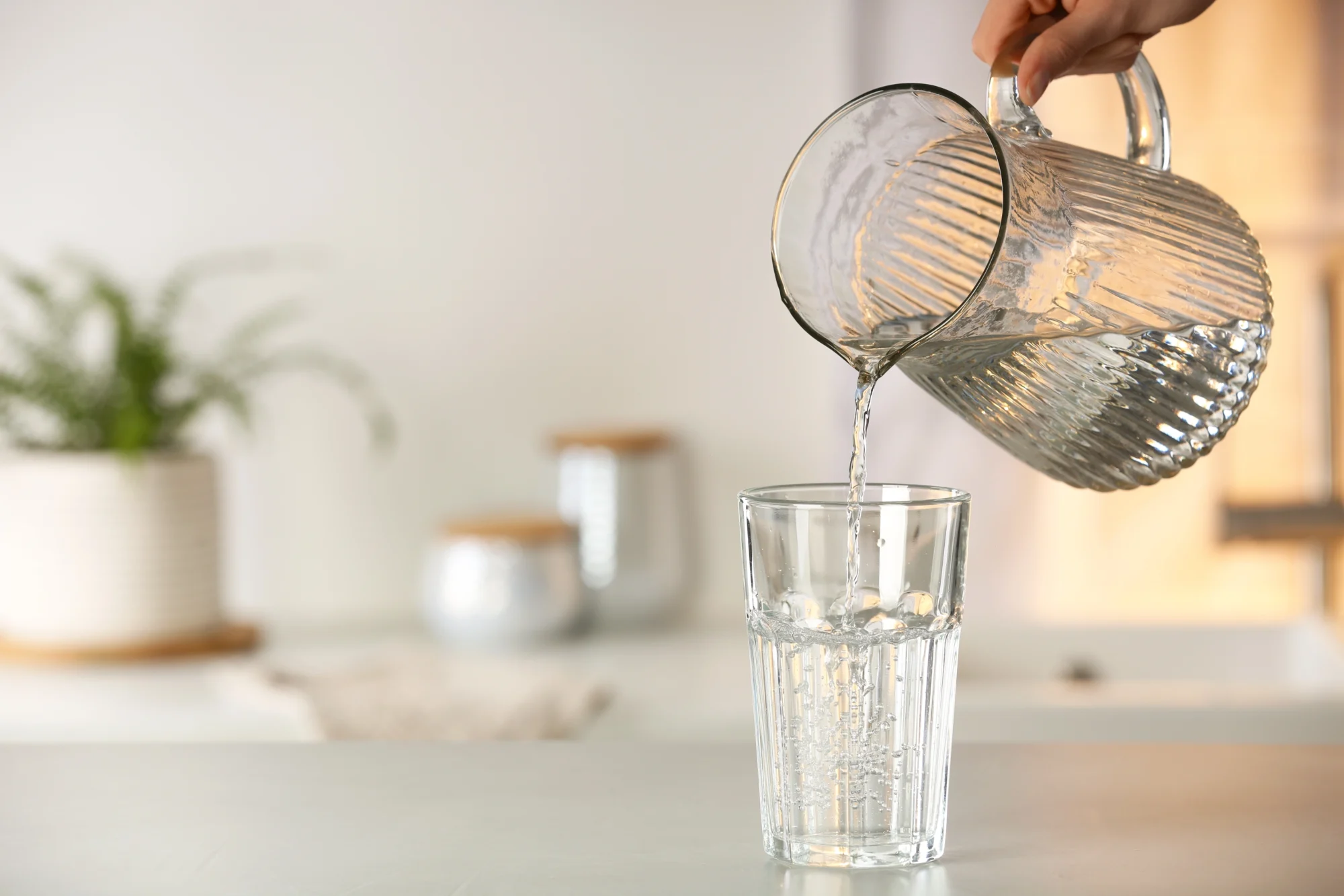 Water is being poured from clear pitcher into clear glass.